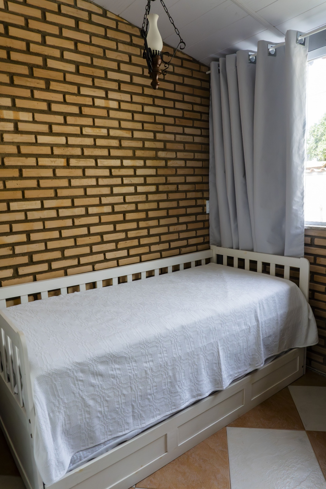 Quarto Tainha — cama de solteiro com parede de tijolinhos e cortinas