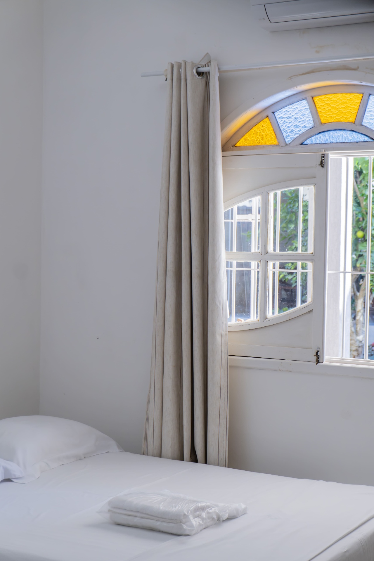 Quarto Cavalinha — cama com toalhas e janela em arco aberta